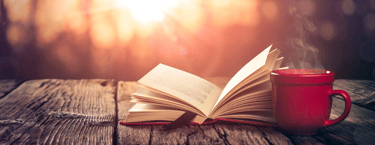 A book and cup of coffee on a table outside.