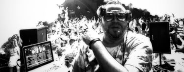 Professional DJ wearing headphones and glasses performing a live set for a crowded dance floor.