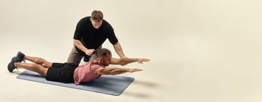 A fitness trainer assisting a man performing a back extension exercise on a yoga mat.