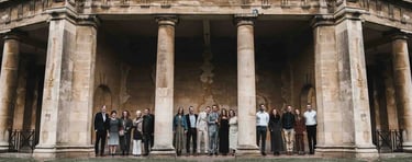 Wedding guests pose between columns of a historic stone pavilion during a luxury garden wedding.