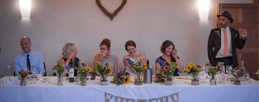 Smiling wedding guests at a head table decorated with sunflowers and a Mrs and Mrs bunting banner.