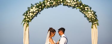 gli sposi dopo la cerimonia, abbracciati sotto un arco floreale di rose bianche che decorava il luogo della cerimonia