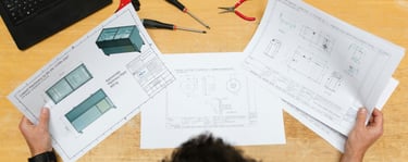 Engineer reviewing technical machine blueprints and CAD drawings at an industrial workstation with tools.