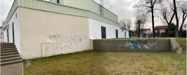 Industrial white building with graffiti on the exterior wall near a concrete staircase and grassy area.