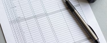 Overhead view of an audit checklist with measurement readings filled in, a digital meter and a pen resting beside the document on a clean grey surface, structured table rows partially ticked, cool north-facing daylight, precise and methodical composition