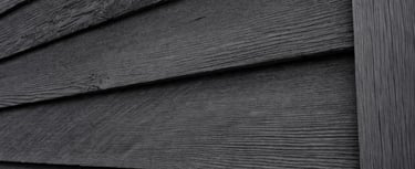 Black wood siding on a traditional barn showing matte, breathable exterior paint aging naturally in shaded conditions