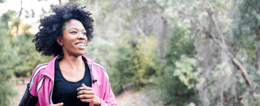 Une jeune femme noire souriante aux cheveux naturels et une veste de sport rose qui fait son jogging