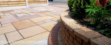 Colourful sandstone paving driveway and curved raised planter with colourful plants and flowers