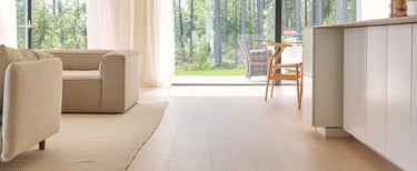 Modern open plan living room featuring light oak hardwood floors and large windows overlooking a forest.