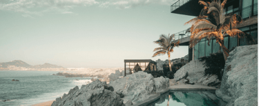 Modern cliffside villa with ocean view, palm trees, and infinity pool at sunset