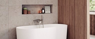 Modern white fluted freestanding bathtub in a luxury bathroom with beige stone tiles and wood wall paneling.
