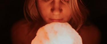 A woman with eyes closed holding a glowing pink Himalayan salt lamp in a dark room.