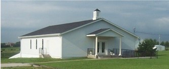 White church building with a black roof and covered porch with blue gray sky and green grass