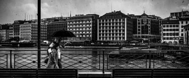a couple of people walking down a bridge over a river in the city of Geneva