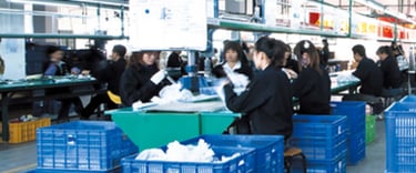 Factory workers in uniform assembling bath products on industrial production line with blue crates.