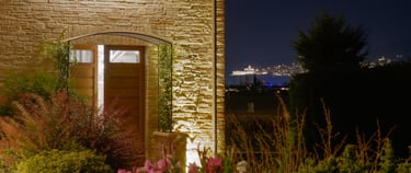 Esterno dell'agriturismo di sera, con fiori del nostro giardino e una romantica veduta su Assisi
