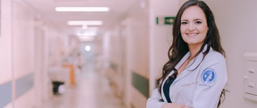 Dra Bruna Melchior de jaleco branco sorrindo de braços cruzados, aos fundos um corredor do hospital das clinicas da USP
