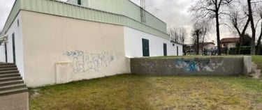 Industrial white building with graffiti on the exterior wall near a concrete staircase and grassy area.
