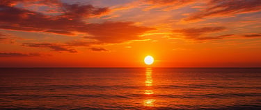 A vibrant orange ocean sunset with red clouds reflecting on the calm beach waves.