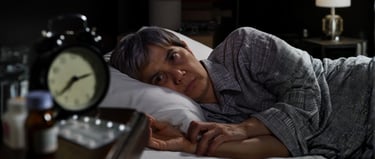Sleepless person with insomnia lying in bed at night next to an alarm clock and medication.