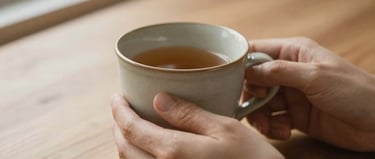 Soft close-up of hands holding a warm ceramic cup on a wooden table, natural light, gentle earth tones, shallow depth of field