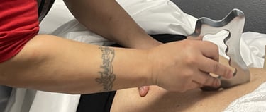 Therapist performing IASTM soft tissue mobilization on a patient's back using a metal scraping tool.