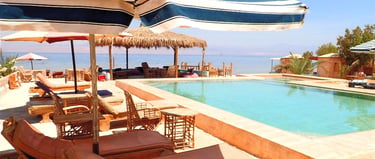 Beachfront pool with blue white umbrellas sunbeds and bungalows at Bedouin Star Egypt.
