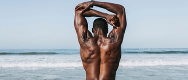 Muscular man stretching his triceps on a sunny beach after an outdoor workout session.