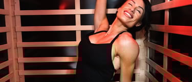 Smiling woman in black athletic wear enjoying a red light therapy session in a modern infrared sauna.