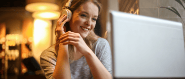a woman in a gray sweater and headphones on a laptop