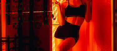 Smiling woman in sportswear standing by a red light therapy panel for skin health and recovery.