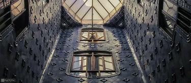 View upward through Casa Batlló’s tiled light well where daylight cascades toward the central skylight.