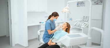 Una dentista con mascarilla y uniforme azul examinando la boca de una paciente 