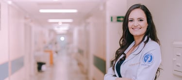 Dra Bruna Melchior de jaleco branco sorrindo de braços cruzados, aos fundos um corredor do hospital das clinicas da USP