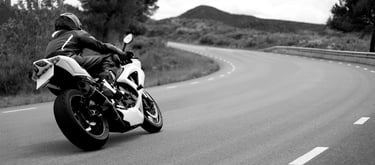 Rear right view of a motorcycle as it take a left hand bend with a road position that gives the view