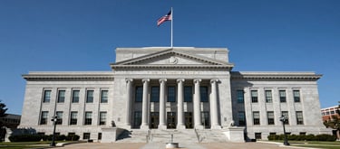 A wide-angle photography shot of a classic US courthouse exterior with a large flag and clean, symmetrical architecture, symbolizing justice and civic responsibility under a clear blue sky.