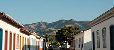 A wide photography shot of a quiet street in Teófilo Otoni, Minas Gerais, with Brazilian architectural style and mountains in the distance, clear blue sky.