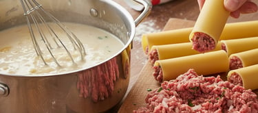 Stuffing dry cannelloni pasta tubes with raw ground meat next to a pot of creamy bechamel sauce.