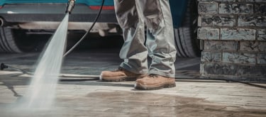 Professional worker using a high-pressure washer to clean a stone paver driveway.