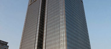 Exterior shot of a modern glass skyscraper in a South Asian / Indian city business park, dusk lighting, warm gold highlights and steel blue shadows, looking professional and established.