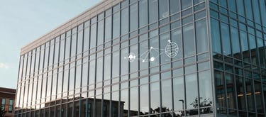 A wide-angle photography shot of a modern glass-and-steel university building facade during a clear afternoon in North America. Reflective surfaces showing global connectivity symbols. Muted blue and grey tones.