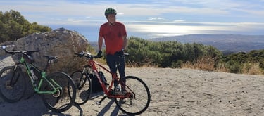 a man standing  with green and red mountain bikes on top of the mountain