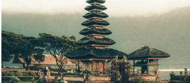 Traditional Thai temple with layered rooftops set against misty mountains and tropical trees at dawn