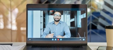 A laptop screen showing a video call with a man in a business shirt holding a pen