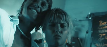 A smiling man and woman posing for a selfie in a blue-lit nightclub with a menu board.