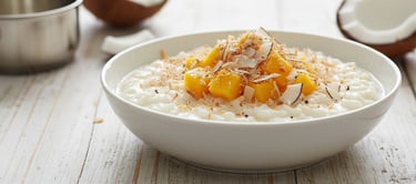Creamy homemade coconut rice pudding topped with mango and toasted coconut, served in a bowl on a wo