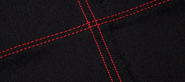Gritty close-up texture shot of heavyweight black cotton fabric with raw red stitching, direct flash, high contrast, harsh shadows