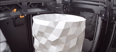 Bambu Lab 3D printer creating a white geometric low-poly vase with an industrial extruder.