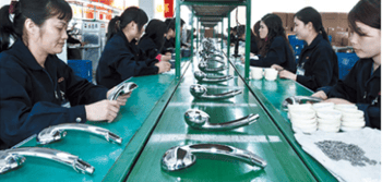 Factory workers assembling chrome shower heads on a green production line conveyor belt.