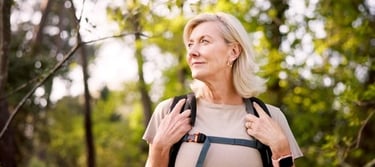 An active senior woman hiking in a sunlit forest with a backpack and smartwatch.